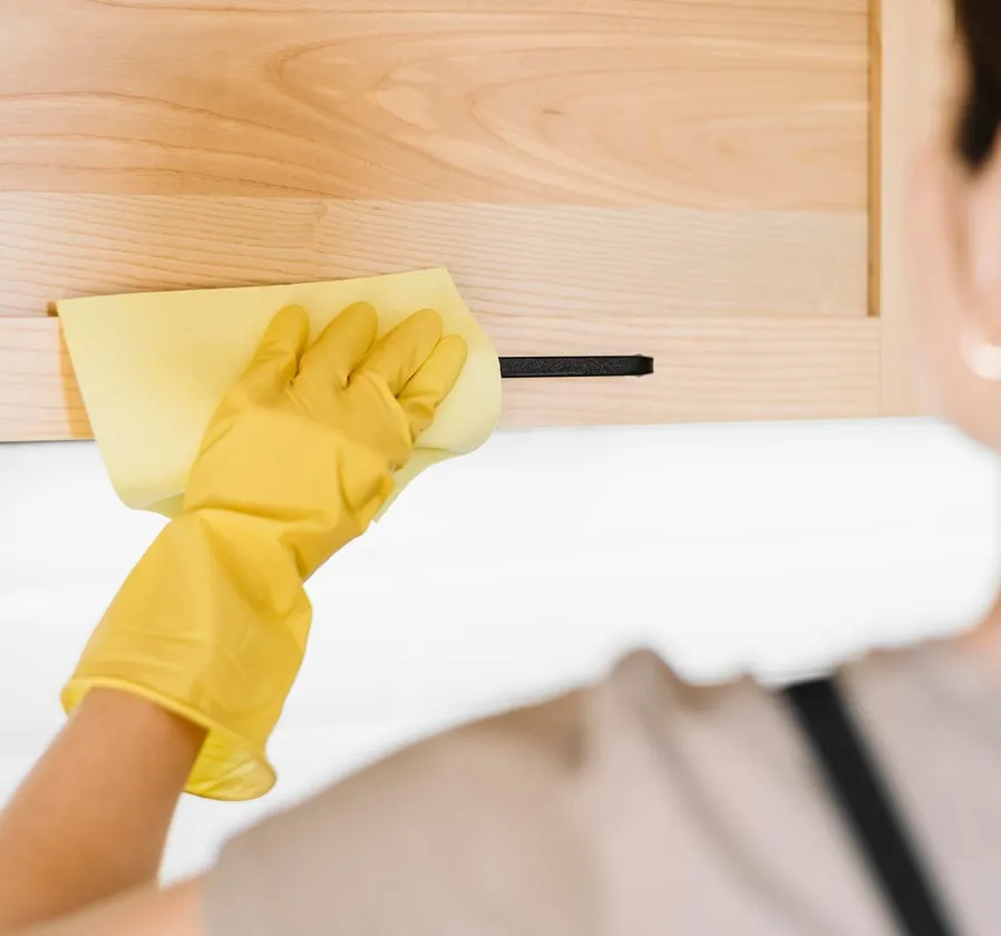 Gloved hand wiping a wooden headboard with a cleaning cloth